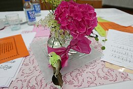 Ein geschmückter Tisch mit einer roten Hortensienblüteeiner Vogelfigur und Liedblättern