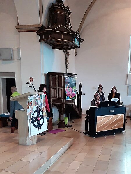 Weltgebetstag 2023 in der Ludgerus-Kirche in Elte: Frauen vor dem Altar mit selbst gestalteten Plakaten.