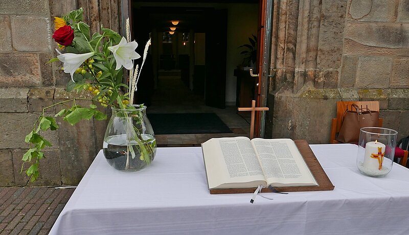 Der Altartisch mit Blumenvase, Kreuz, Bibel und Kerze vor der Kirchtüre
