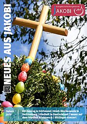 Titelseite Osterbrief Jakobi, Holzkreuz über einem Buchsbaumstrauß, der mit bunten Eiern verziert ist.Dahinter eine Baumkrone und blaer, leicht bewölkter Himmel