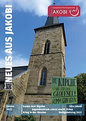 Titelbild Gemeindebrief Ostern 2022: Jakobi-Kirchturm und ein grünes Plakat Plakat mit der Aufschrift " Die Kirche hat für Dich geöffnet. Komm gern herein!"