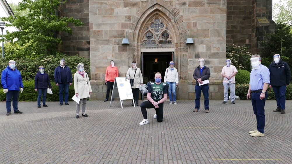 Vor dem Eingang zur Jakobi-Kirche steht das Ordnerteam mit aufgesetzten Gesichtsschutzmasken. Vorne in der Mitte kniend der "Rheine-Raptors Defensive Tackle" Christoph Middelhoff.